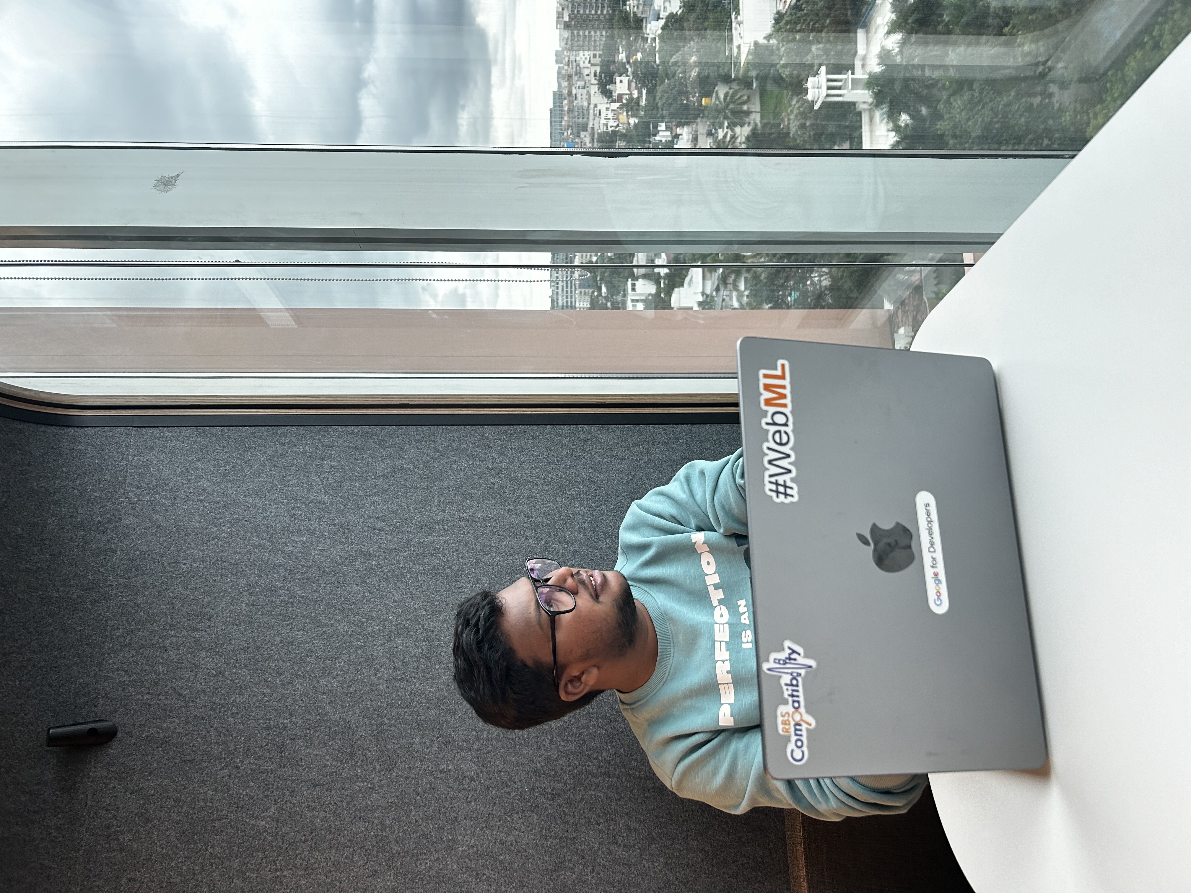 Shabul Hussain coding on MacBook with WebML sticker at office window