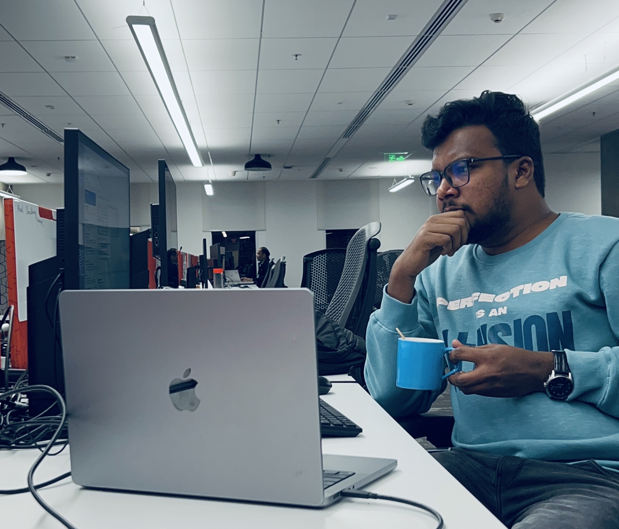 Shabul Hussain Abdul deep in thought at JPMorgan Chase office with MacBook and coffee