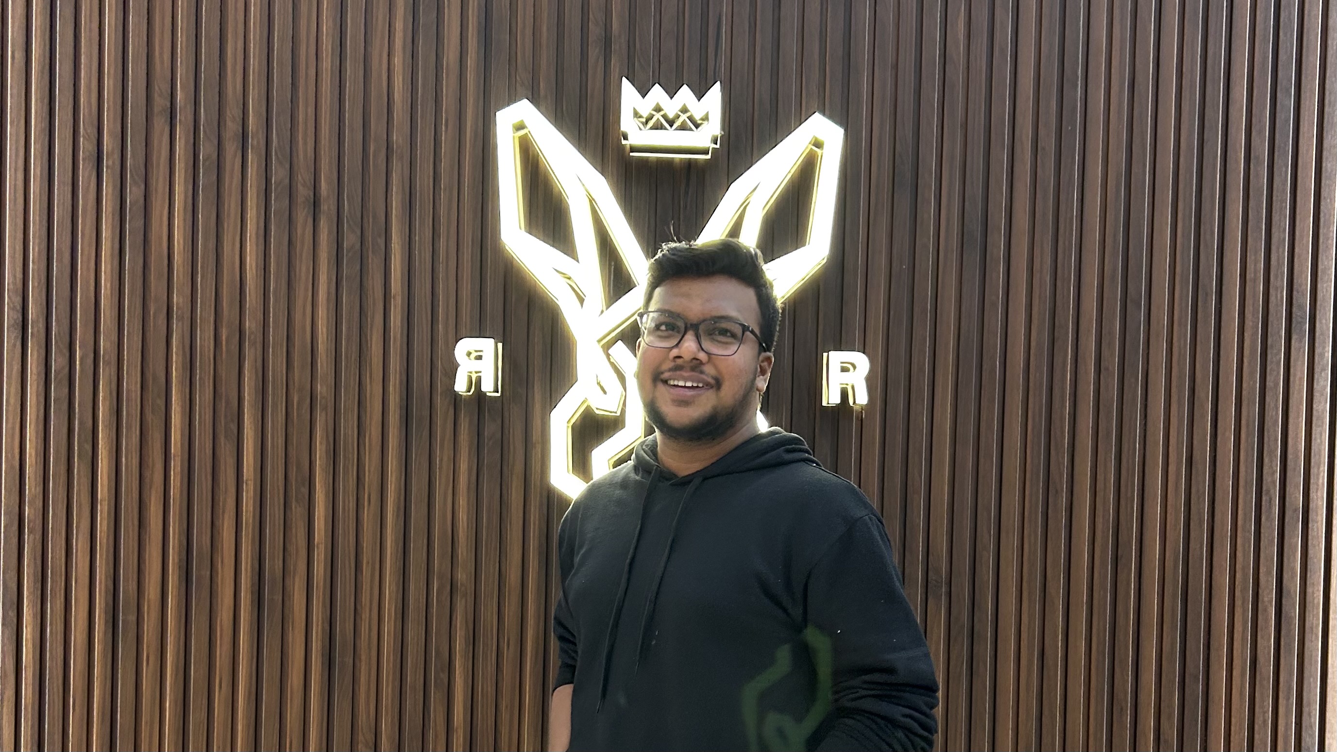 Shabul Hussain smiling in front of neon crown logo wall